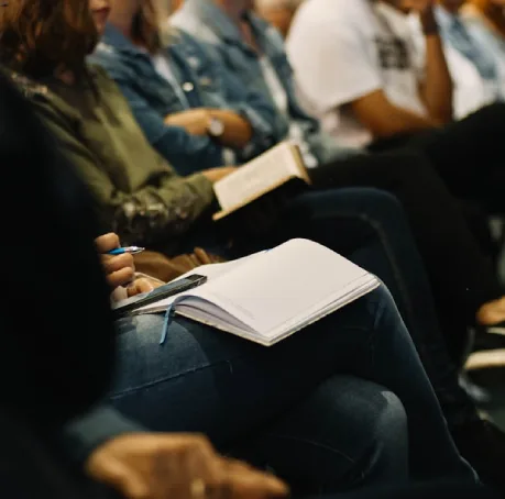 Personas toman notas en un cuaderno durante una reuni&oacute;n o conferencia.