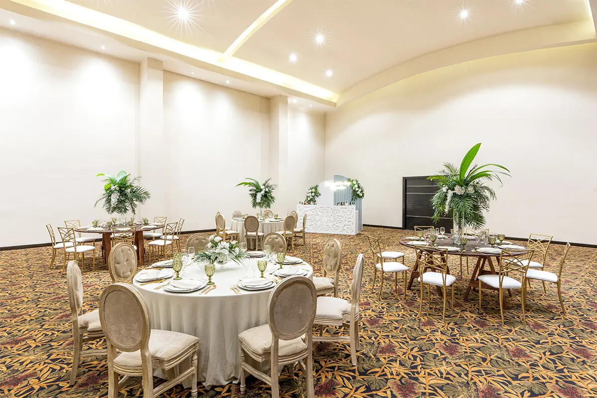 Elegant banquet hall with floral table settings, gold chairs, and palm decor