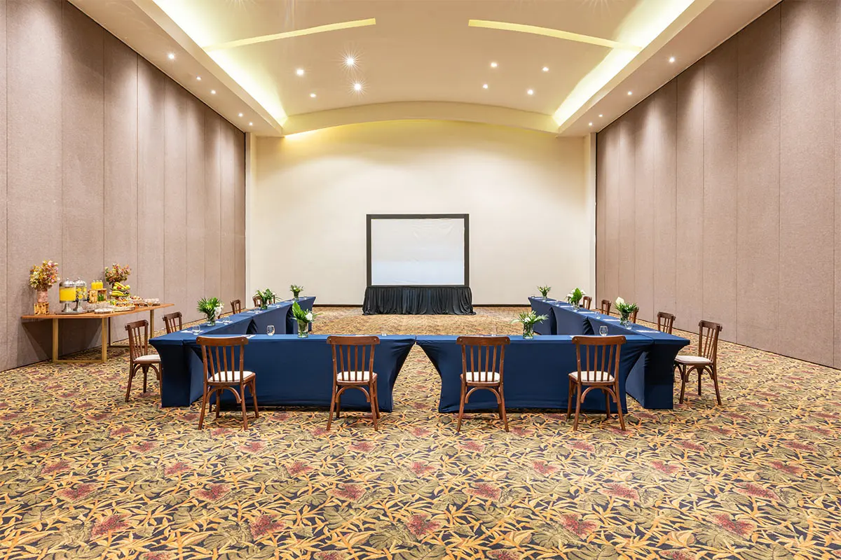 Conference room setup with stage, screen, blue table, and chairs, banquet decor