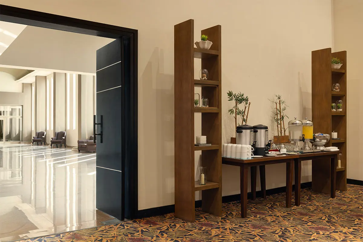 Modern hotel buffet setup with coffee machines and plants in wooden shelves.