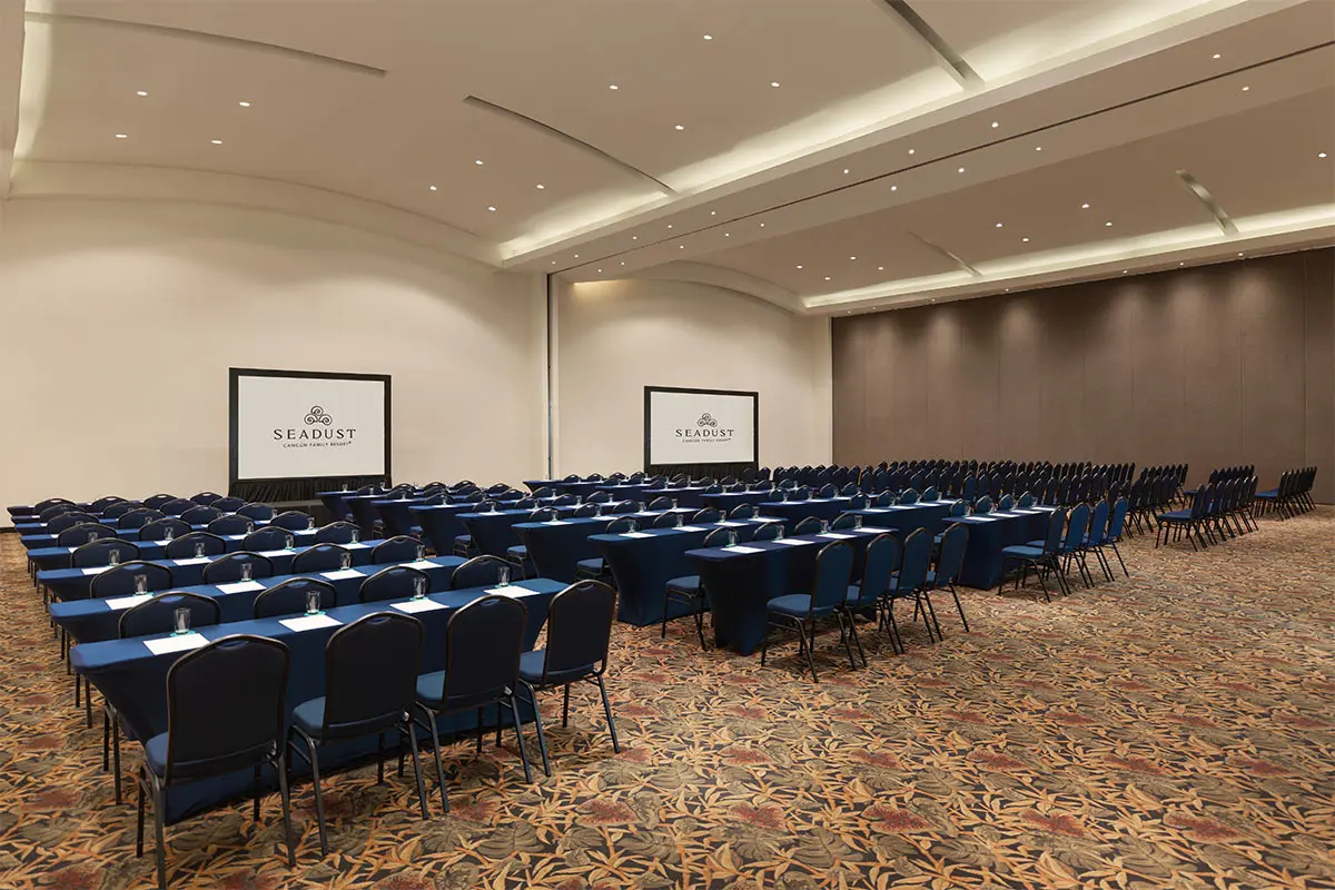 Hotel conference room with rows of blue chairs and tables under recessed lights