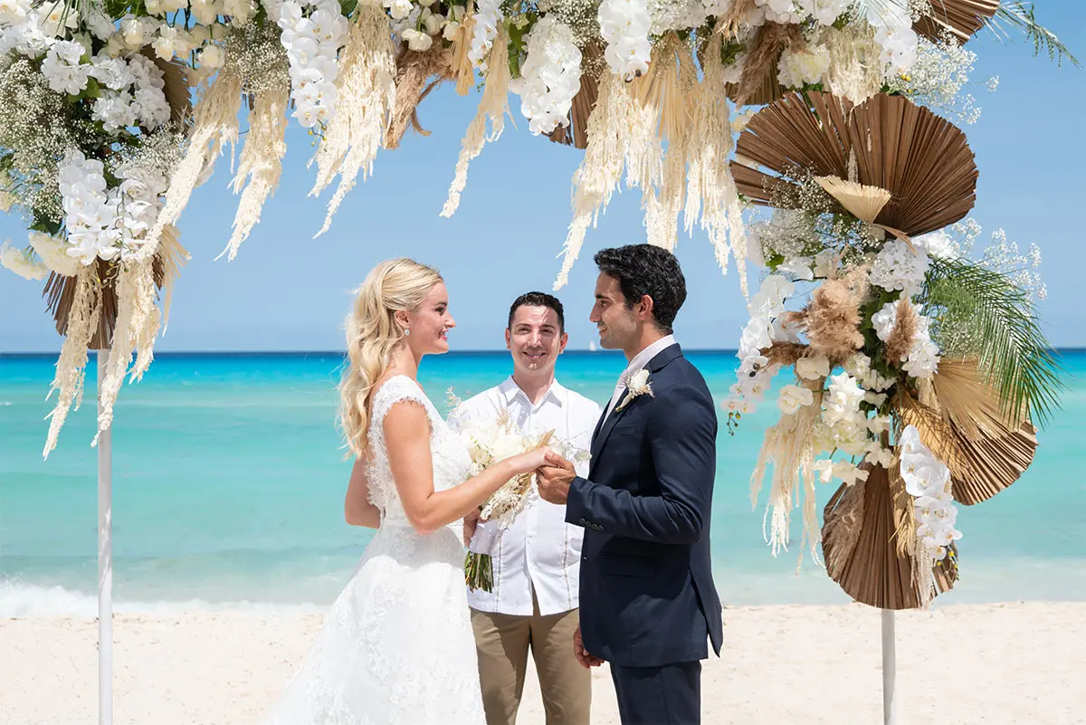 Bride and groom exchanging vows on a beach under ornate floral arches