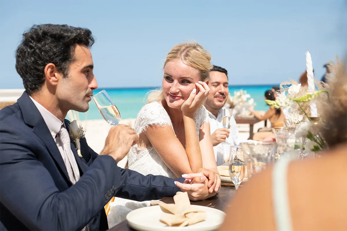 Wedding guests toast at seaside table with woman smiling in white dress