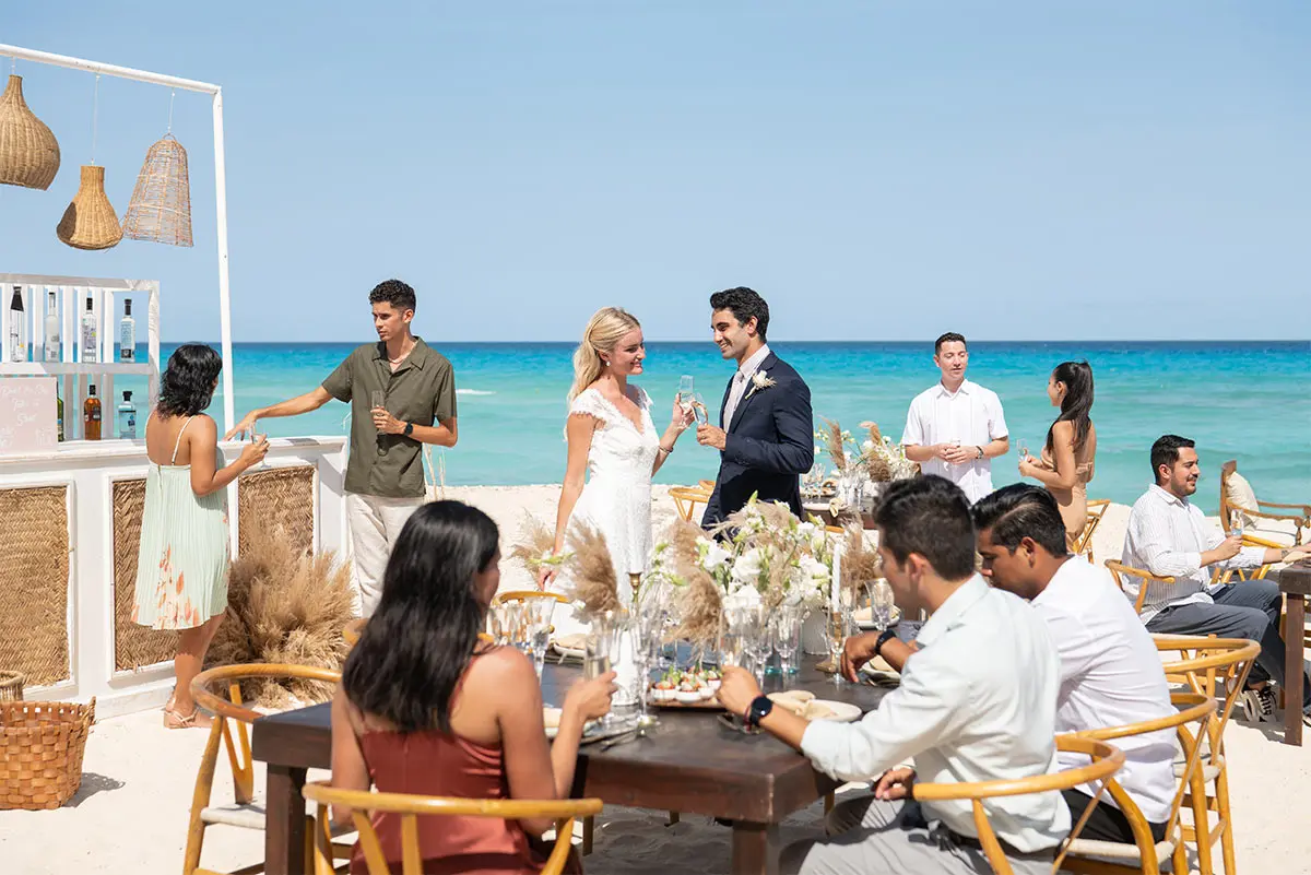 Wedding reception with guests dining and toasting on a beachside table