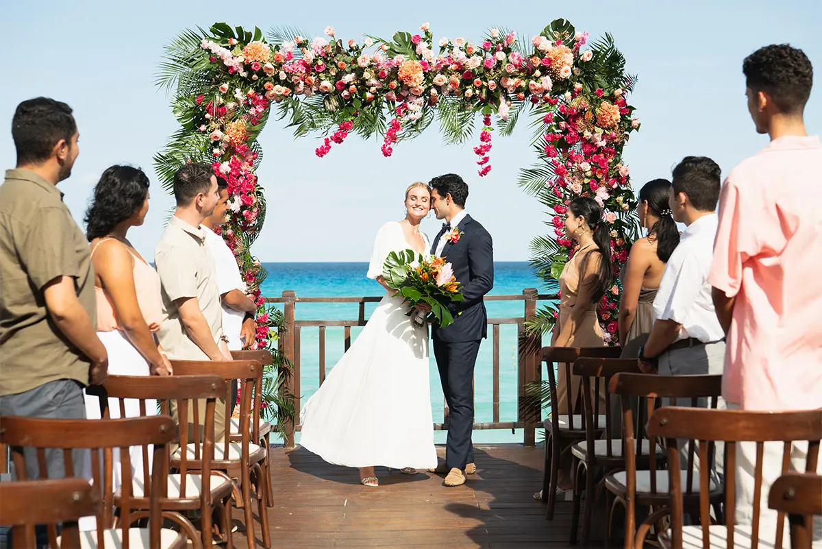 Wedding couple exchanging vows under a floral arch on a seaside deck ceremony