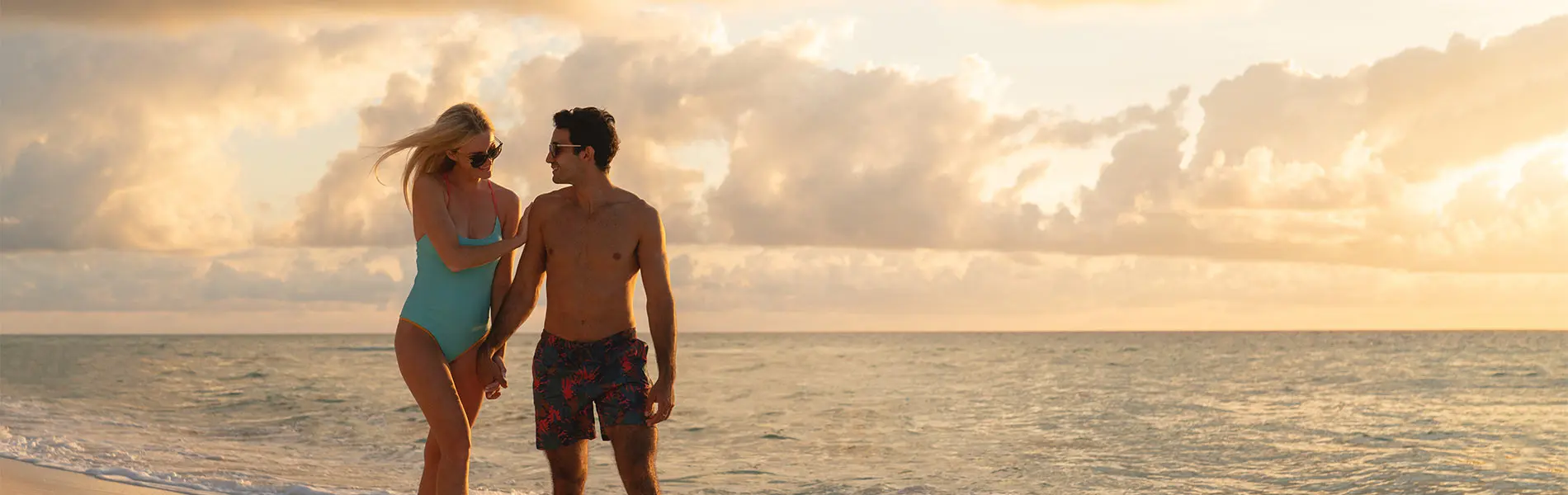 Couple walking on beach at sunset, holding hands and smiling