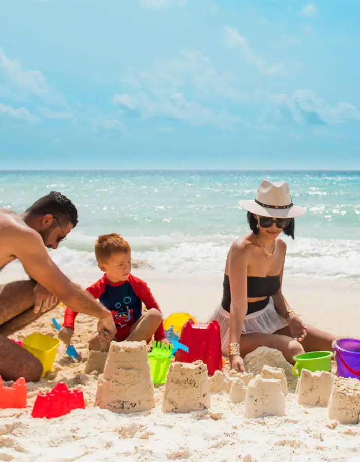 Family building sandcastles on a sunny beach, with colorful toys nearby