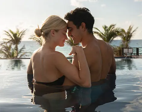 Couple kissing in a pool at sunset with palm trees in the background