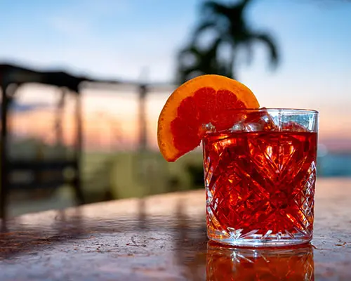 Red drink cocktail with an orange garnish on a seaside table at sunset
