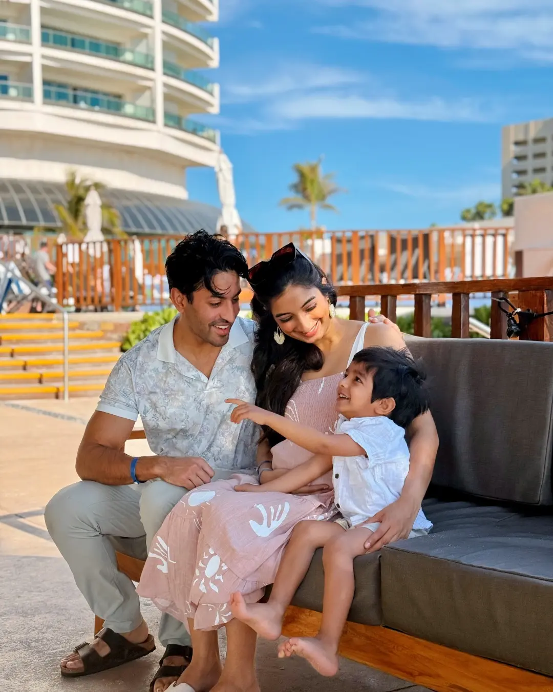 Family on outdoor patio, man and woman holding a smiling child near sofa