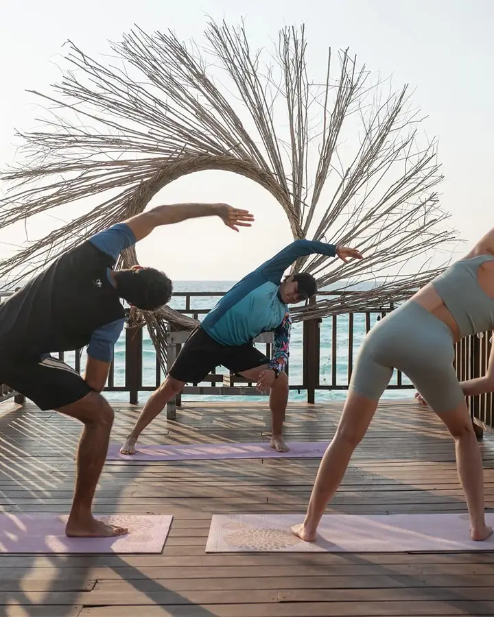 People practicing yoga on mats outdoors on a wooden deck by the ocean