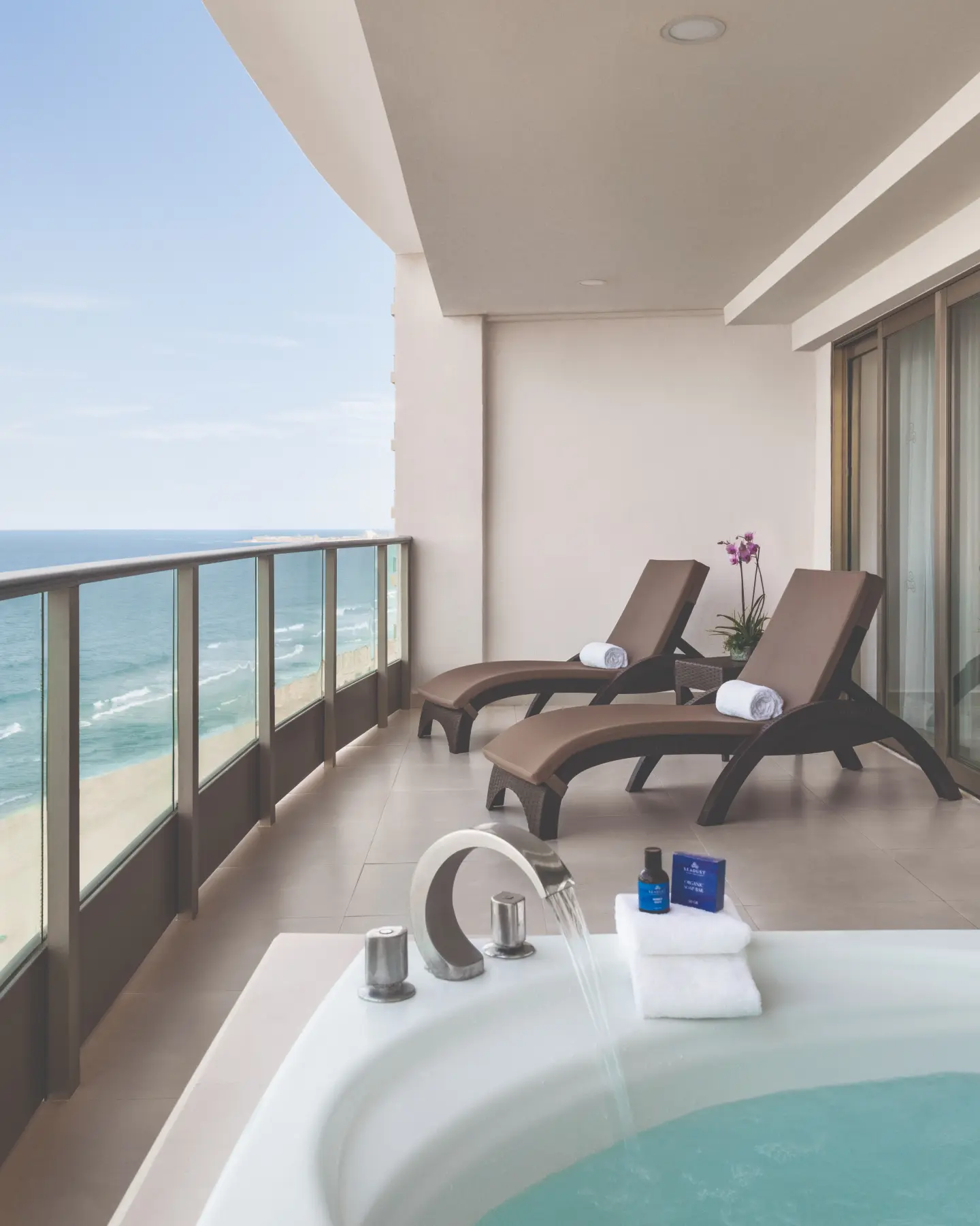 Ocean-view balcony with two lounge chairs, flowers, and a hot tub under a canopy