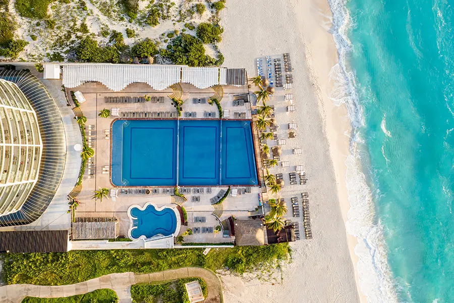 Aerial view of oceanfront resort with blue pools and sun loungers on beach