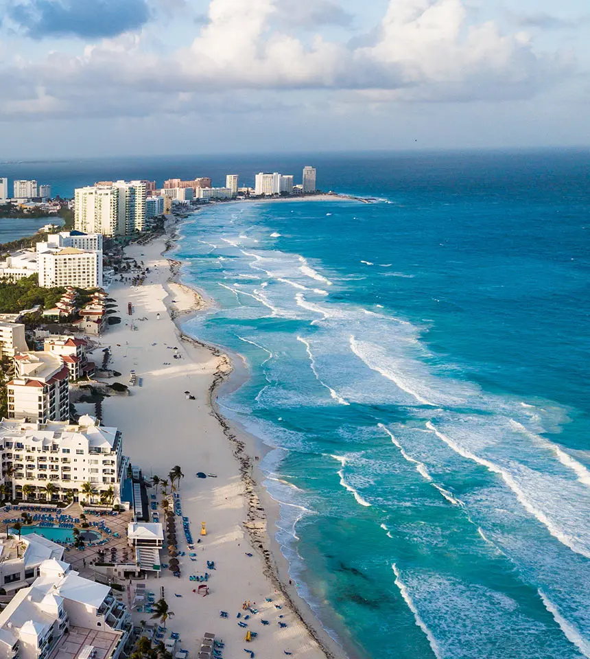 Aerial view of a tropical beachfront with hotels and waves under clouds