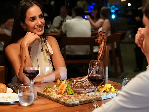Smiling woman at a restaurant table with a carved meat platter.