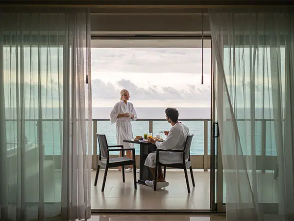 Two chefs in white aprons dine together by a seaside window, daylight.