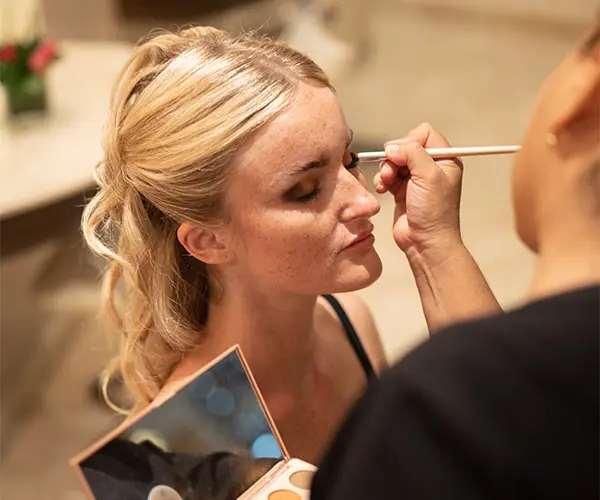 Makeup artist applies eyeliner to a blonde woman in a salon.