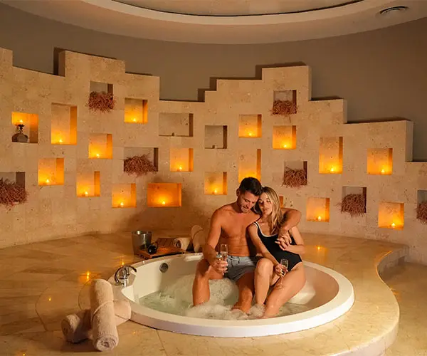 Couple relaxing in a candlelit hot tub with warm wall candles behind them