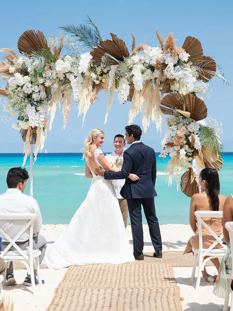 Beach wedding ceremony with floral arch and couple exchanging vows by sea