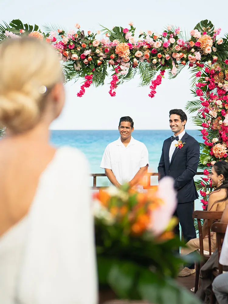 Wedding ceremony with floral arch and guests by the ocean background
