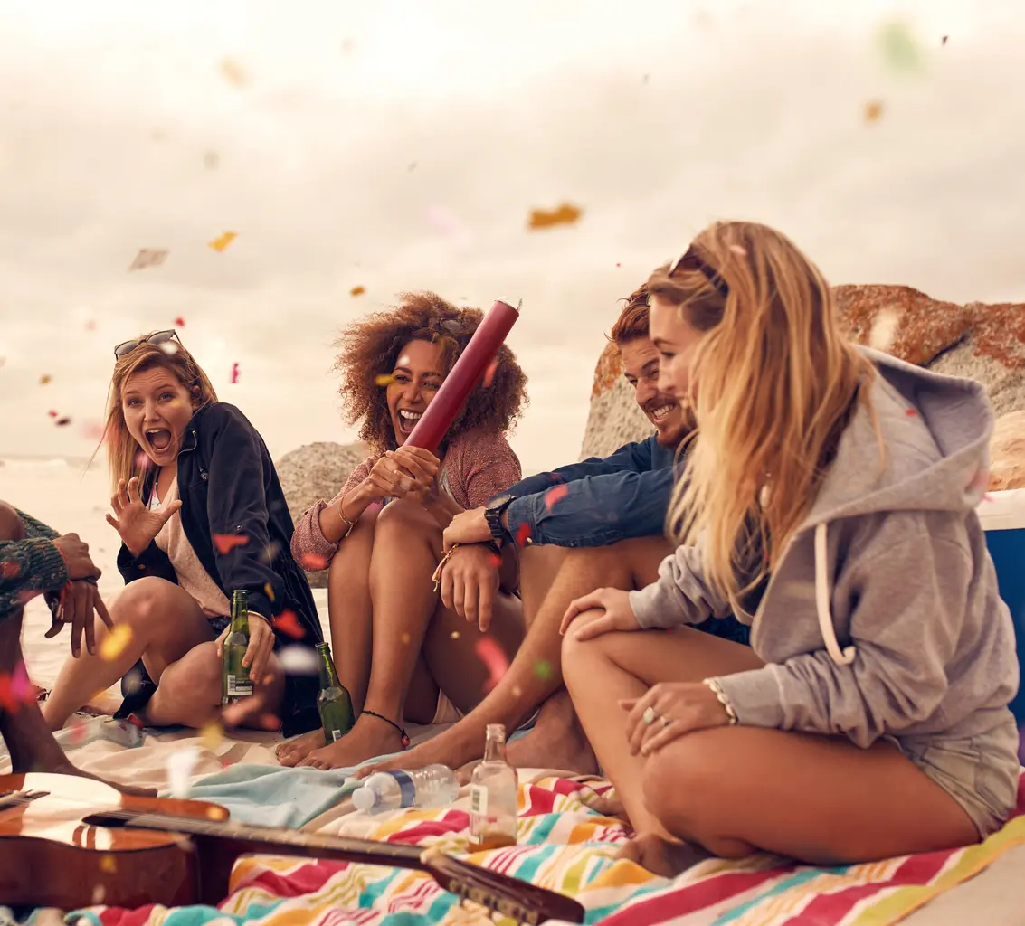 Grupo de amigos celebrando en la playa con confeti y bebidas.