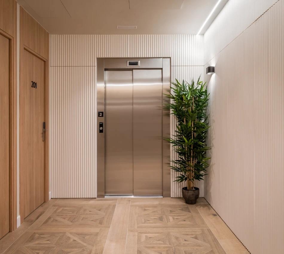 Pasillo moderno con ascensor y planta decorativa. Puerta de habitaci&oacute;n 201.