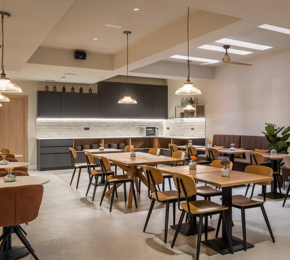Comedor moderno con mesas de madera y l&aacute;mparas colgantes.