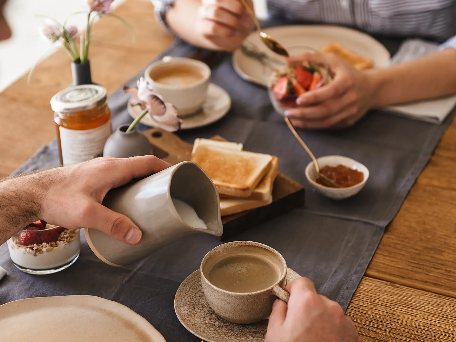 Manos sirviendo caf&eacute; con leche en desayuno con tostadas y yogur.
