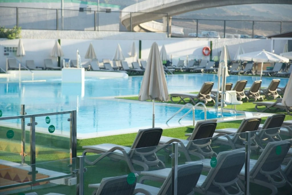 Piscina con sillas reclinables y sombrillas en un entorno moderno y soleado.