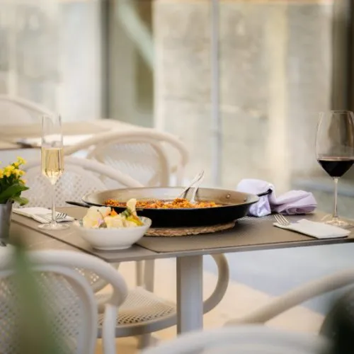 Mesa de comedor con plato, vino y copas al fondo, en interior elegante.