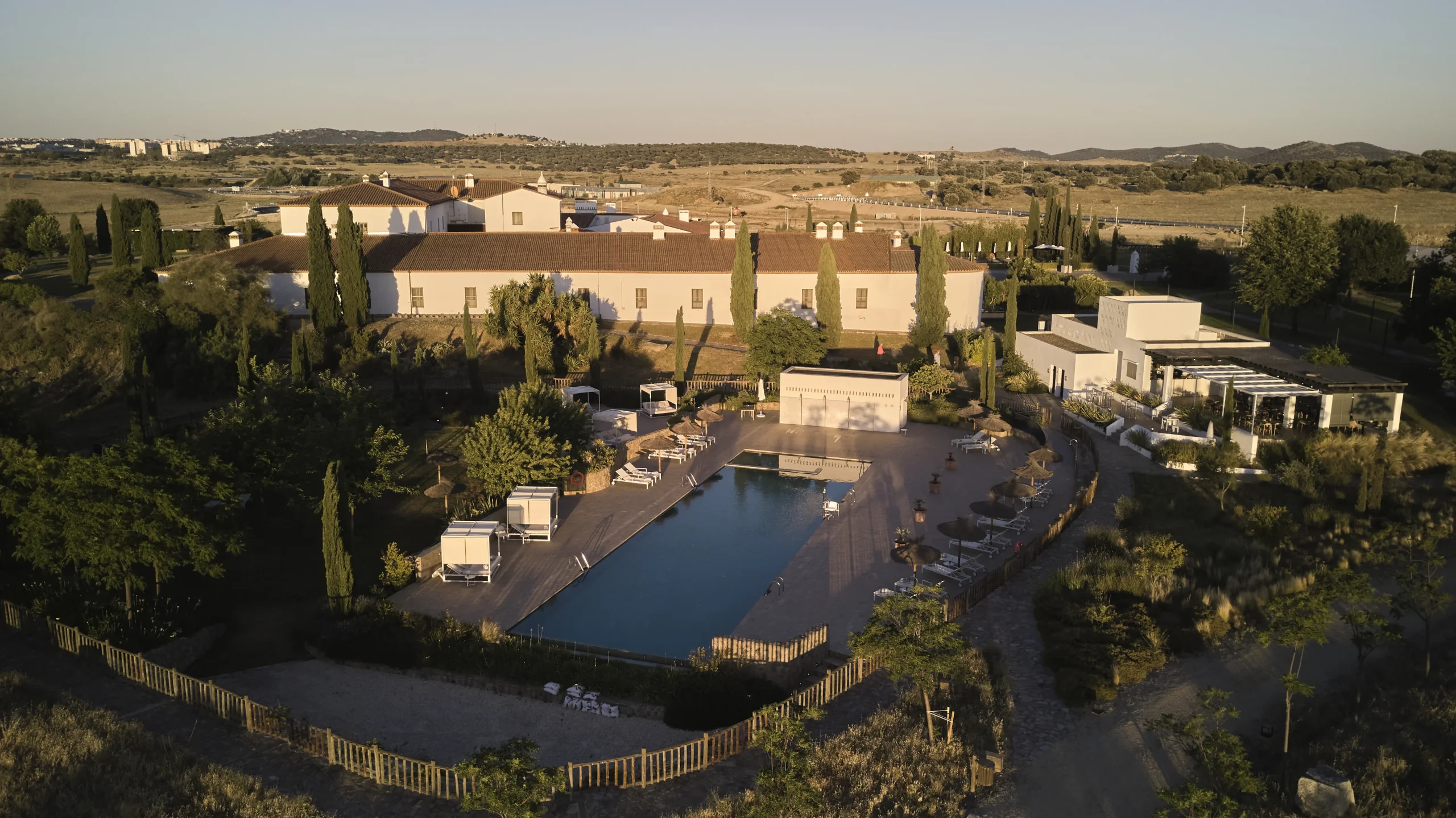 Vista a&eacute;rea de un hotel rural con piscina y jardines entre colinas y olivares