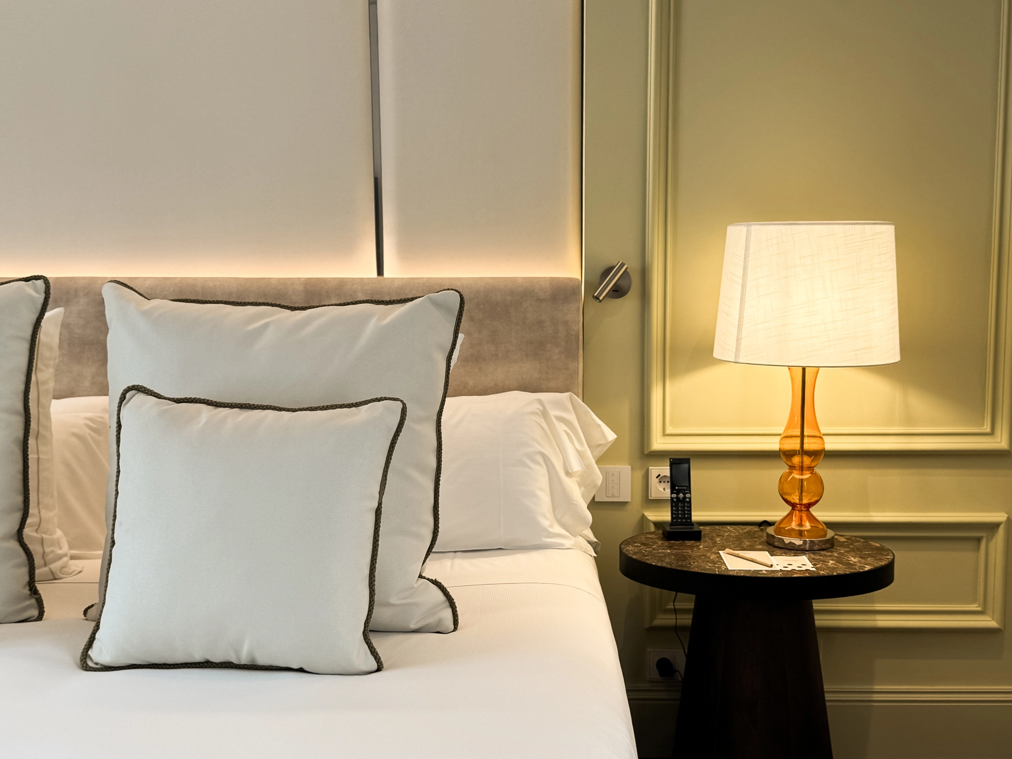 Dormitorio: cama con cojines, mesita y l&aacute;mpara encendida junto a pared con enchufes