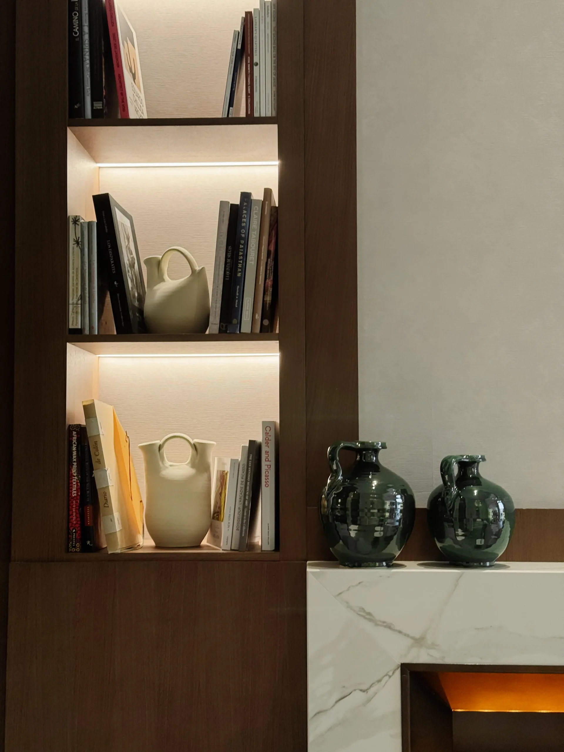 Estanter&iacute;a de madera con libros, jarr&oacute;n y botellas verdes sobre repisa.