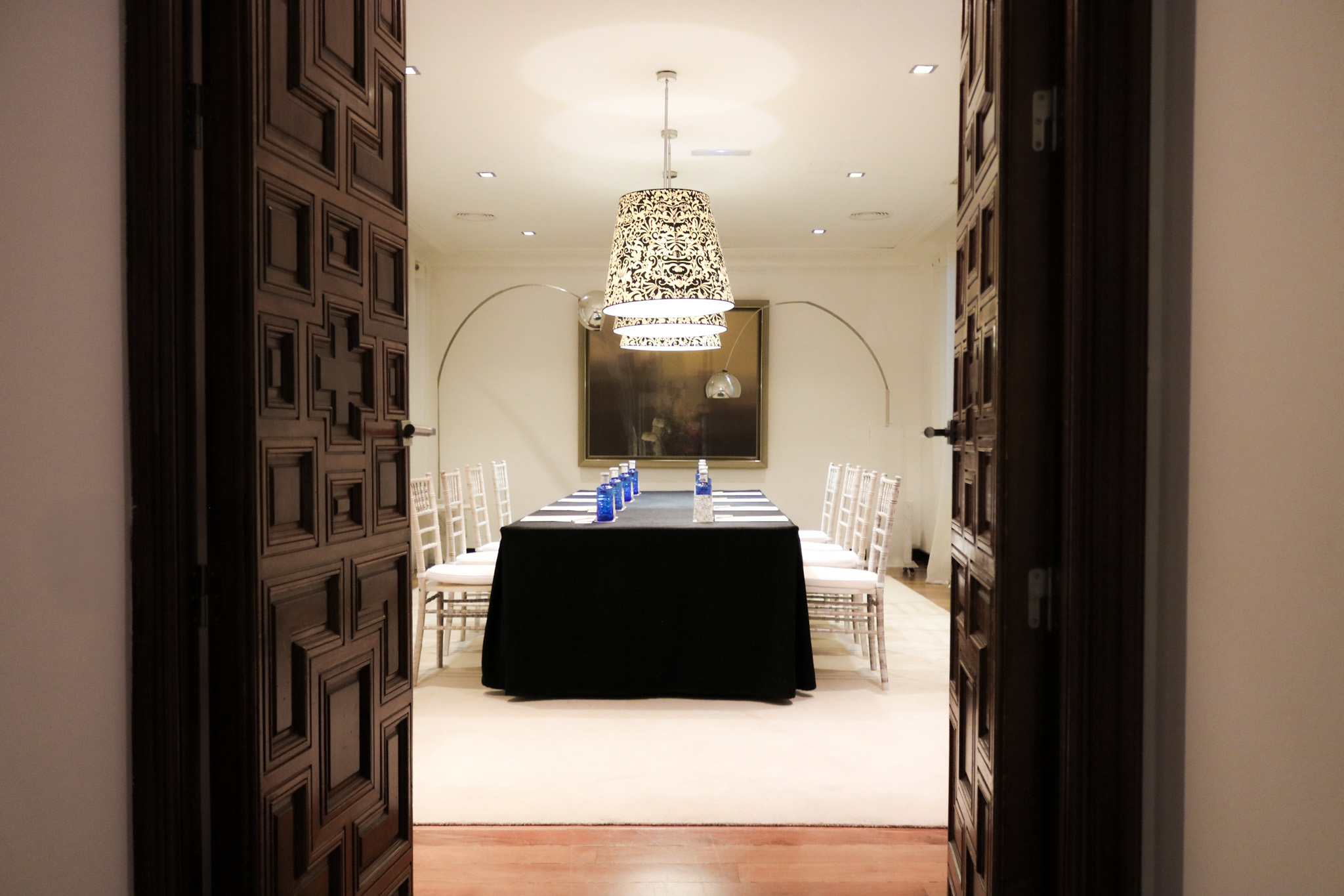 Sala elegante con mesa vestida, l&aacute;mpara colgante y sillas blancas; puertas abiertas