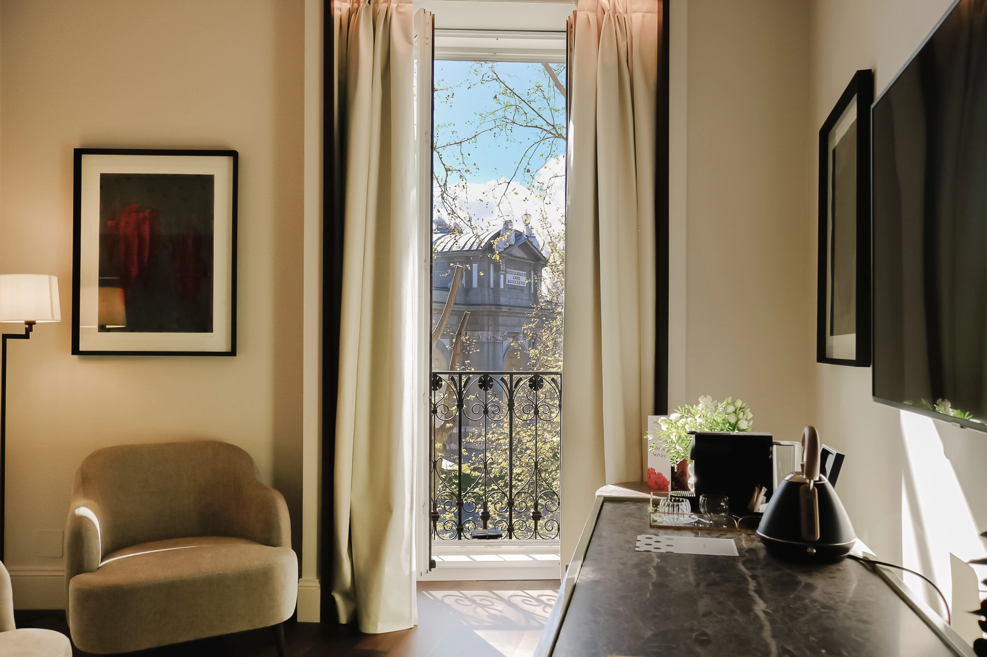 Sala luminosa con sill&oacute;n, cuadros y ventana con vista a un edificio y jard&iacute;n
