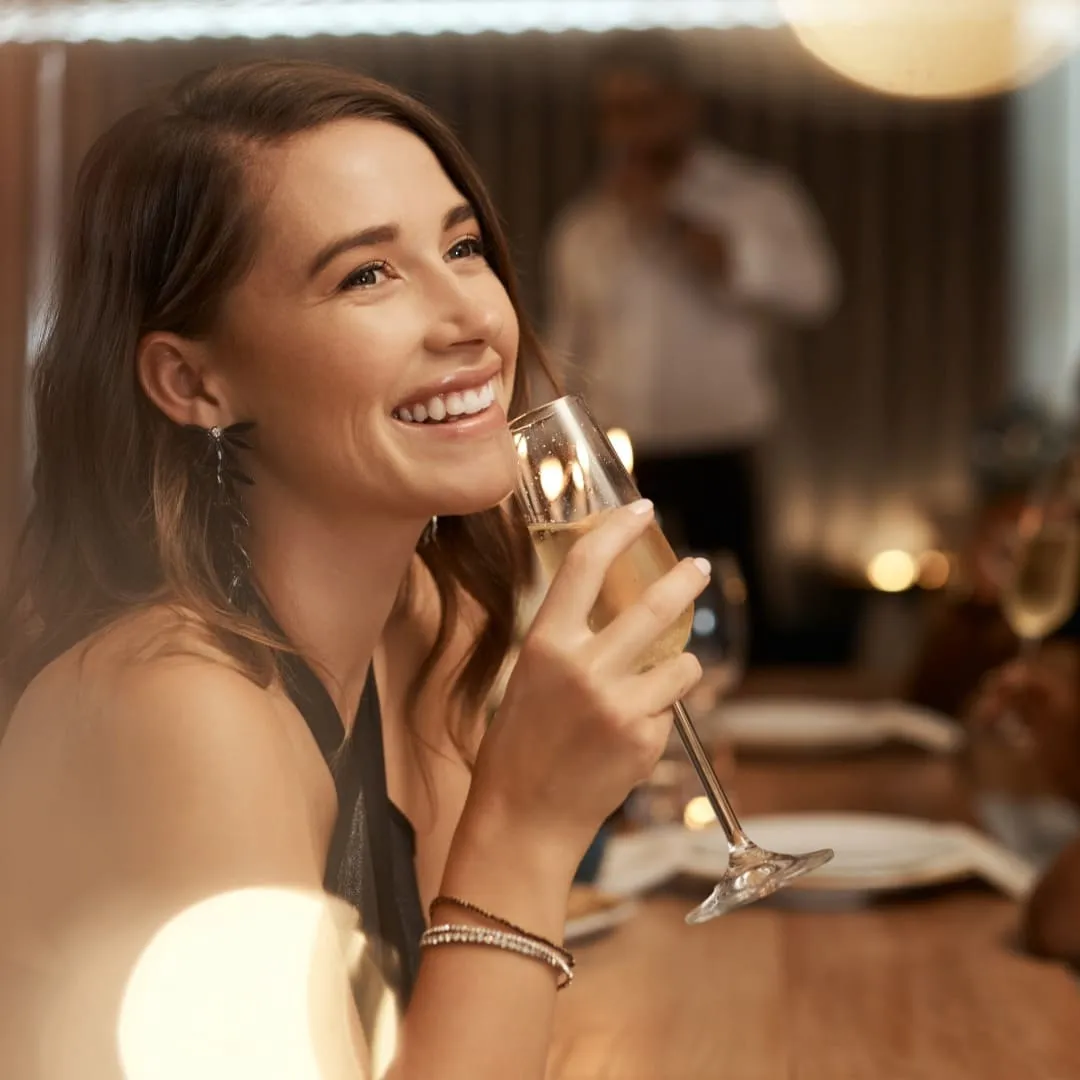 Mujer brindando con copa de champ&aacute;n en un ambiente elegante y c&aacute;lido.