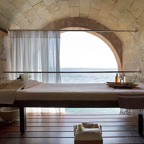 Interior con arco de piedra y ventana al mar, cortinas y botella sobre mesa