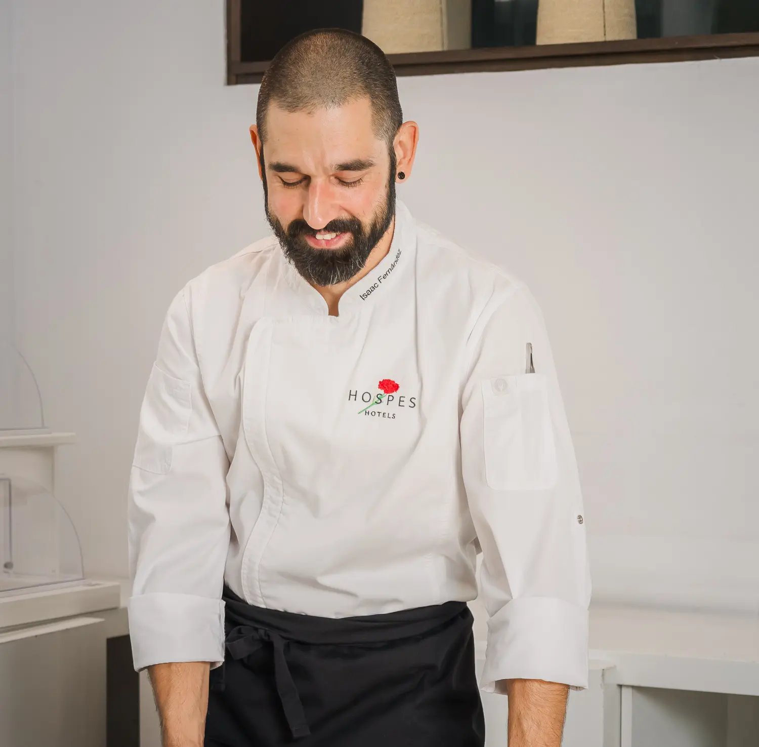 Chef con uniforme blanco y barba, mirando hacia abajo en un hotel