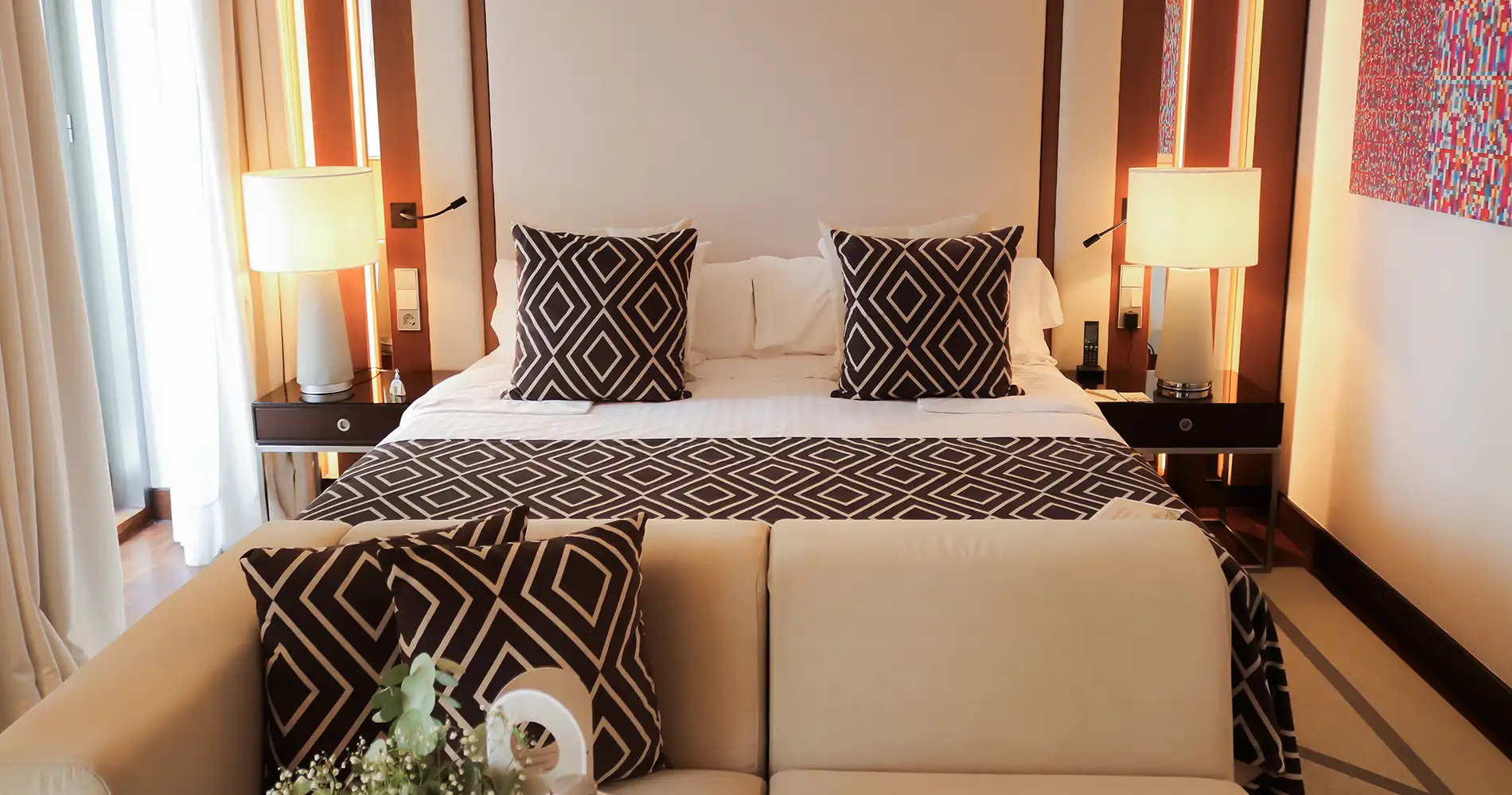 Habitaci&oacute;n de hotel con cama doble y cojines geom&eacute;tricos, l&aacute;mparas y cortinas