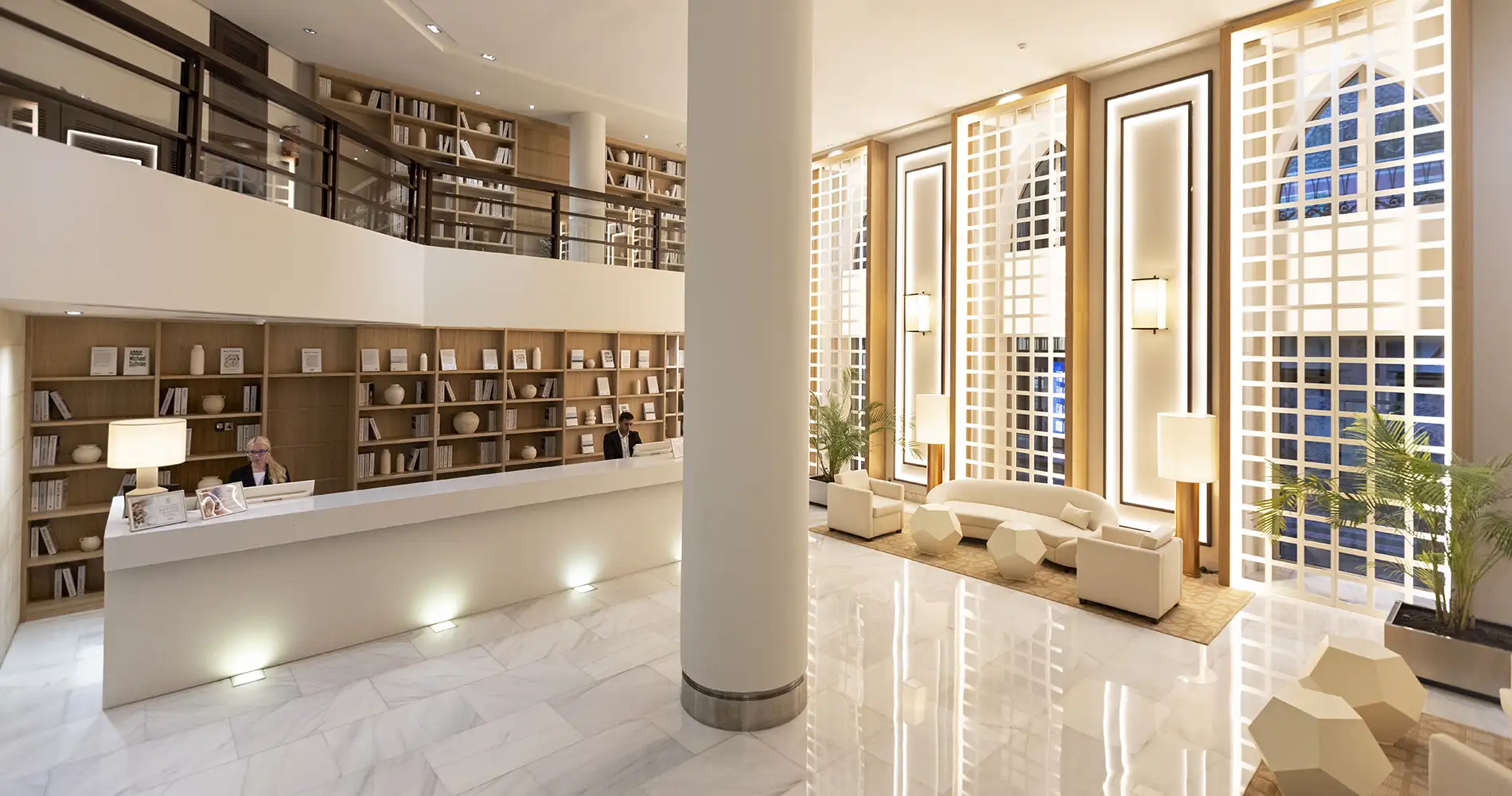 Recepci&oacute;n y sala de espera moderna con bibliotecas y sof&aacute;s blancos, luz natural
