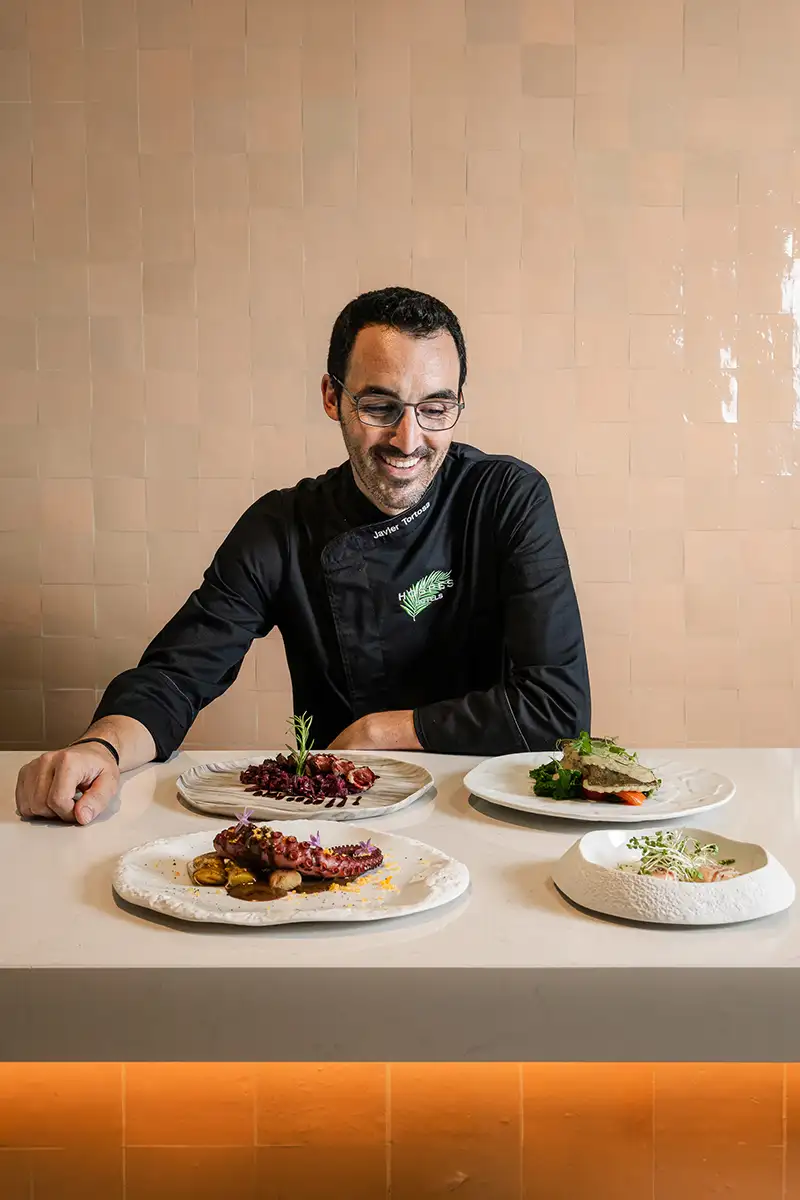 Cocinero sonriente presenta platos gourmet sobre la mesa, en un restaurante
