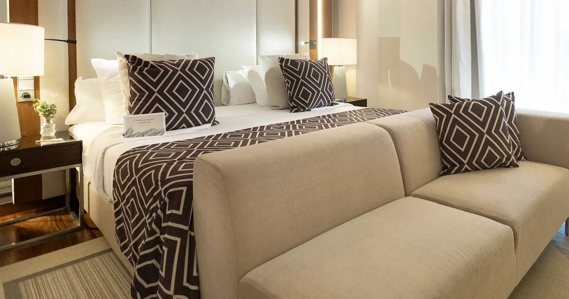 Cama doble con almohadas y mantas de rombos, en una habitaci&oacute;n luminosa
