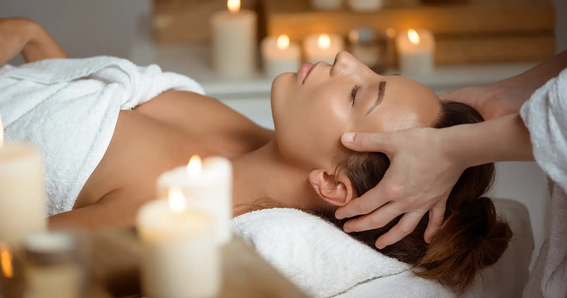 Masaje relajante: manos acarician el rostro de una mujer en spa con velas