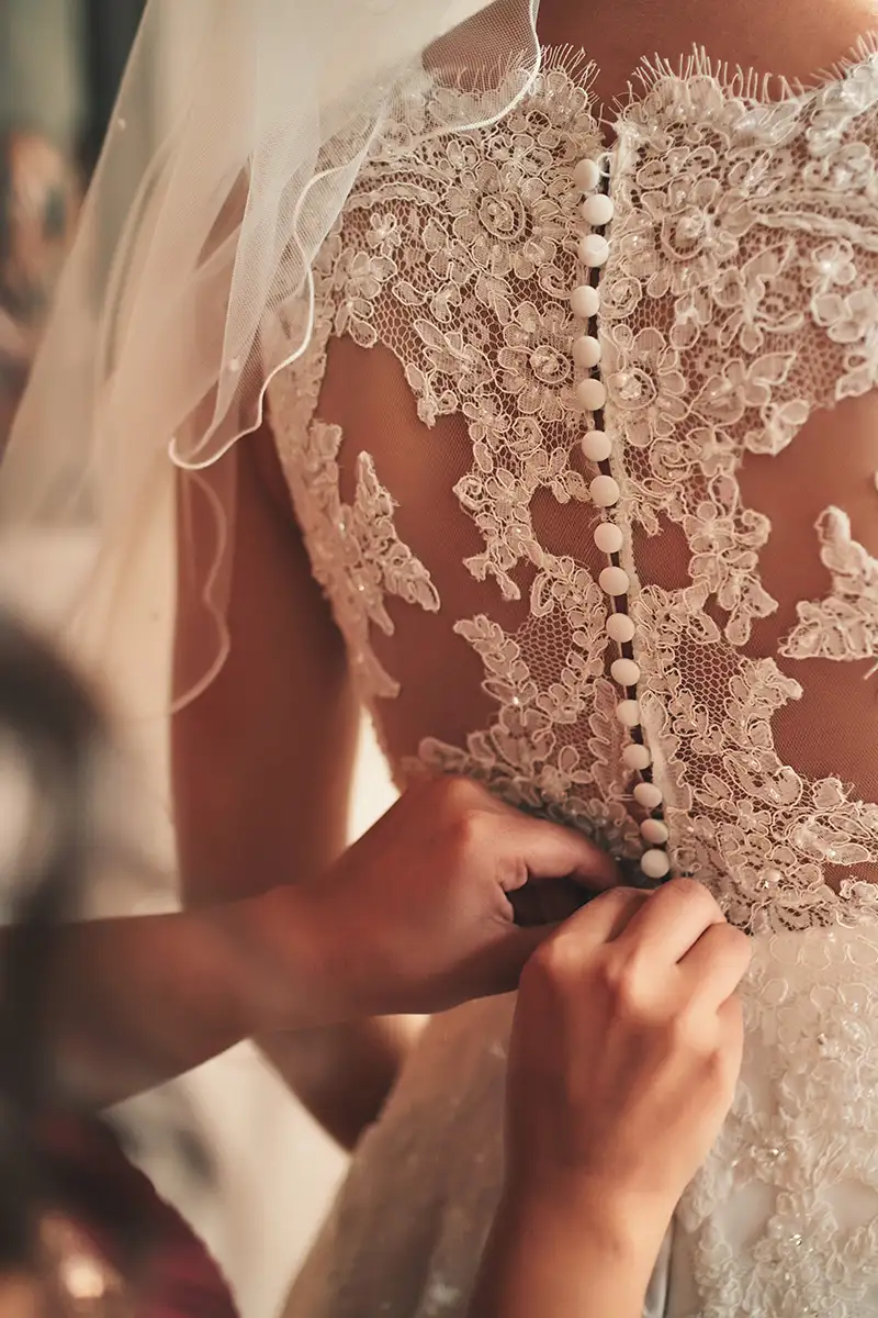 Manos ajustando un vestido de novia de encaje con botones decorativos