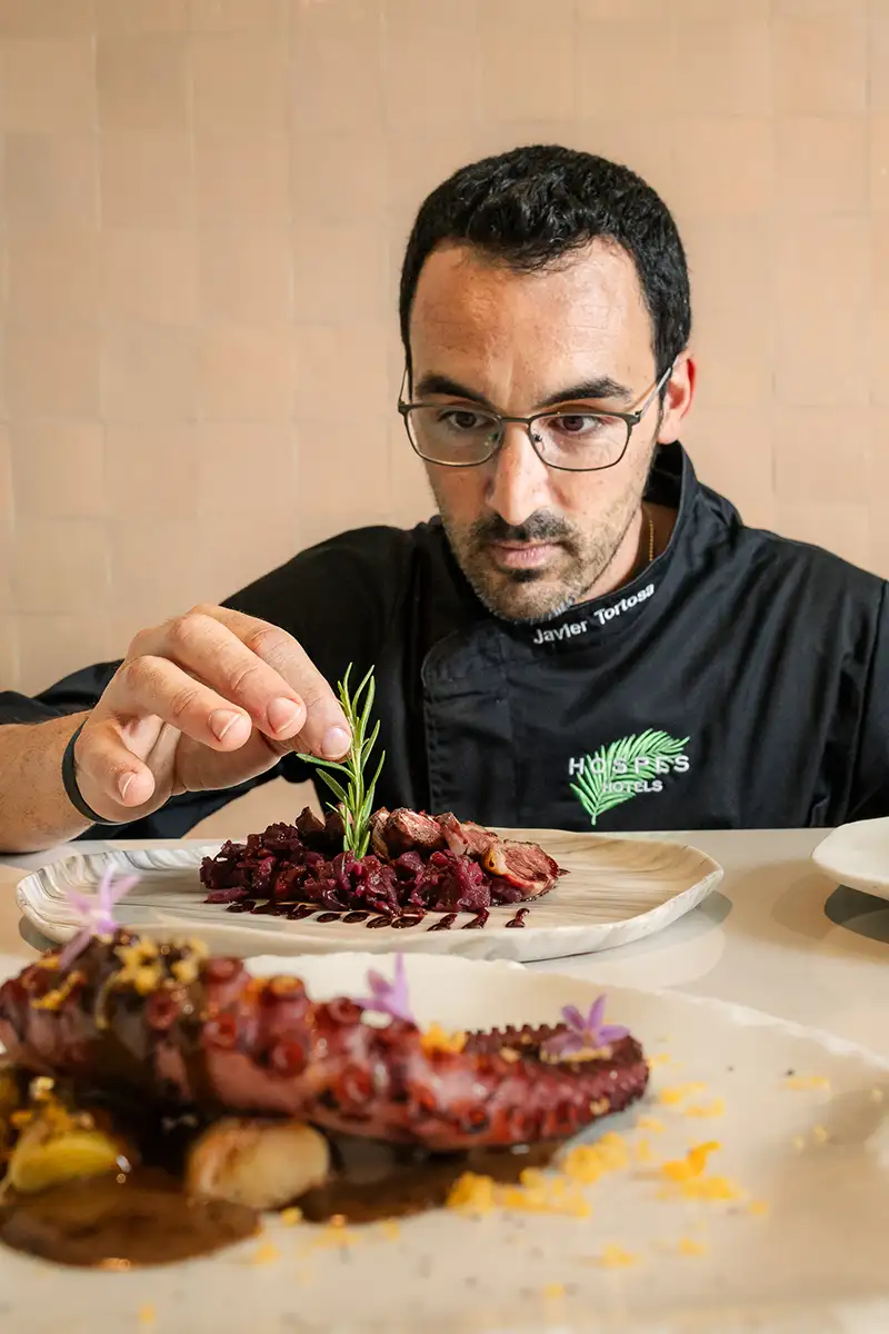 Cocinero con gafas apunta a un plato de carne en restaurante.