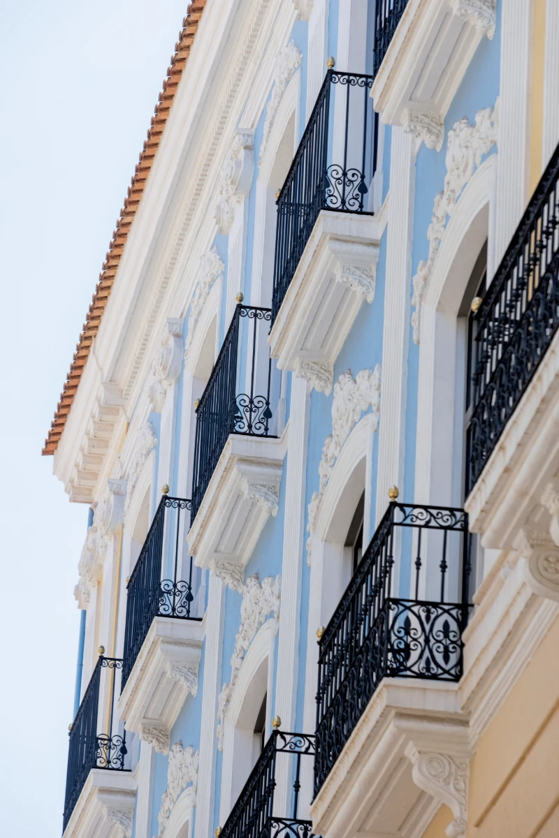 Fachada de edificio colonial con balcones y barandillas negras, azul y blanco.