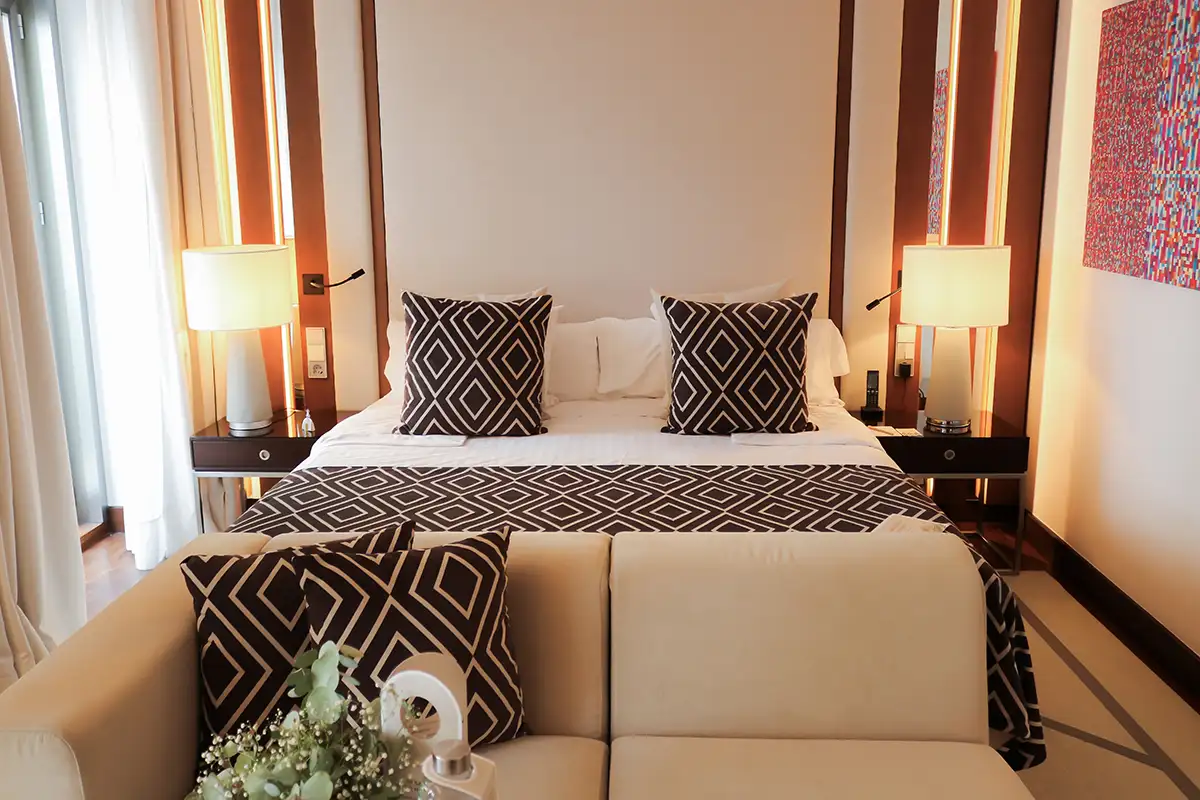 Dormitorio elegante con cama doble y almohadas geom&eacute;tricas, l&aacute;mparas y cortinas