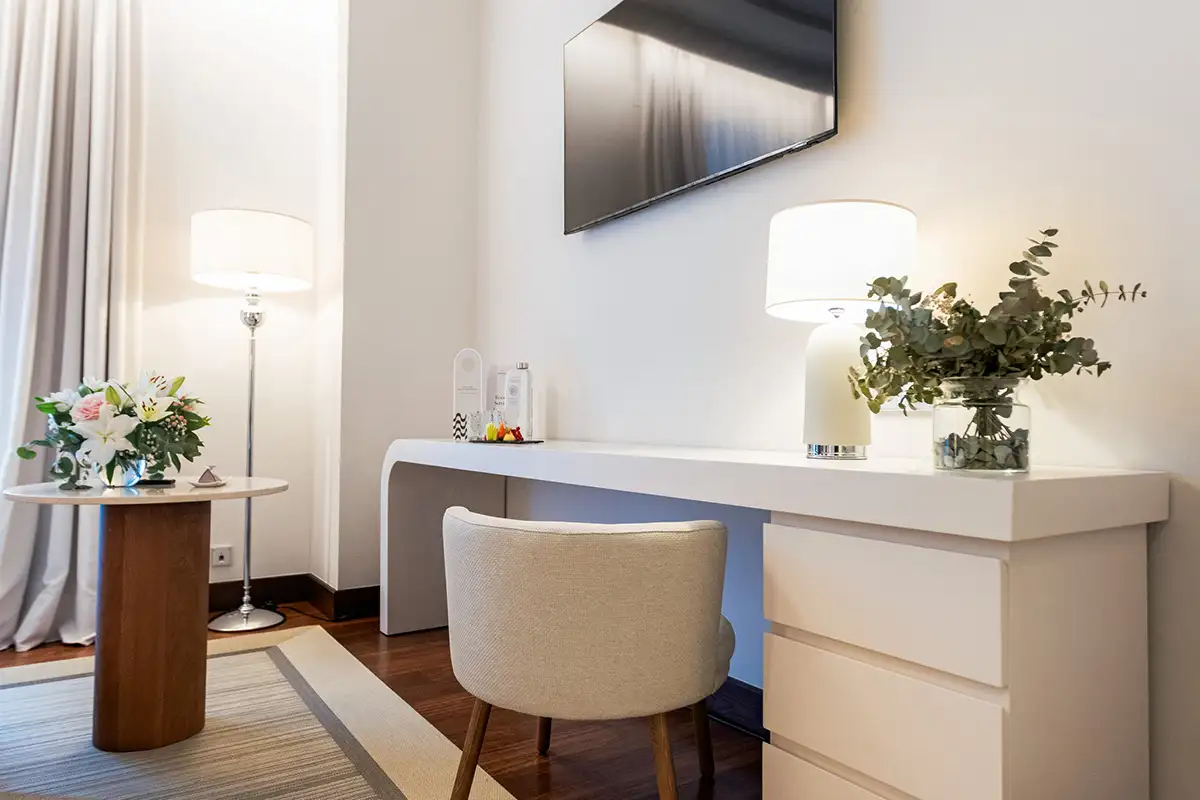Sala moderna con escritorio blanco, l&aacute;mparas y flores decorativas.