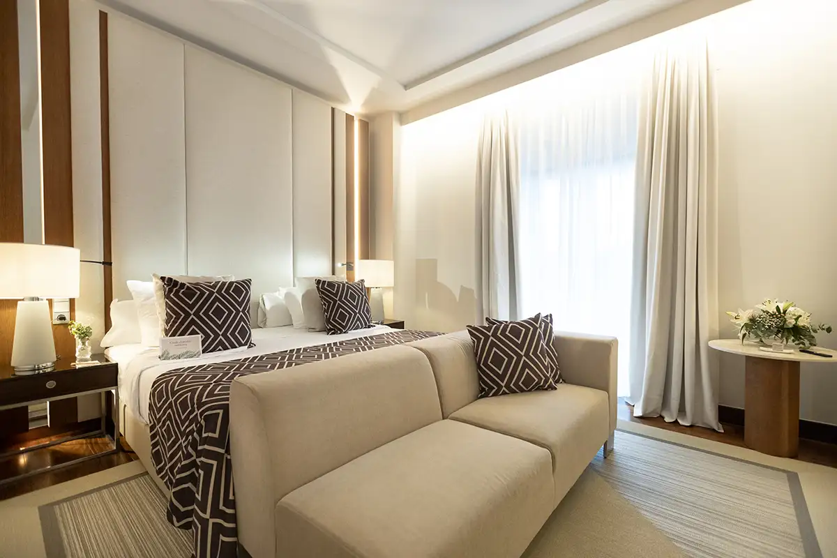 Dormitorio moderno con cama, sill&oacute;n y cortinas claras iluminadas por luz natural