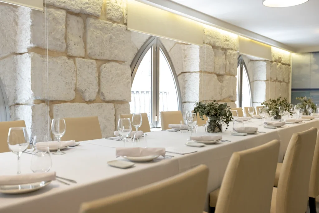 Comedor elegante con mesas cubiertas, copas y flores en ambiente c&aacute;lido.